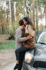 beautiful young couple in love kisses and hugs sitting on a car