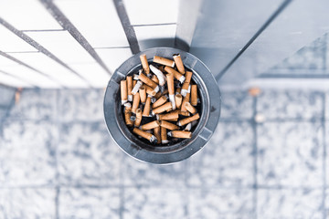 A full ashtray in front of a bright brick wall seen from above.