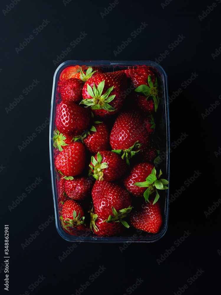 Wall mural Strawberries in plastic container box on black background, from above