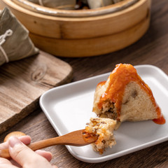 Rice dumpling zongzi eating - Young Asian woman is eating Chinese traditional food on wooden table at home for Dragon Boat Festival celebration, close up