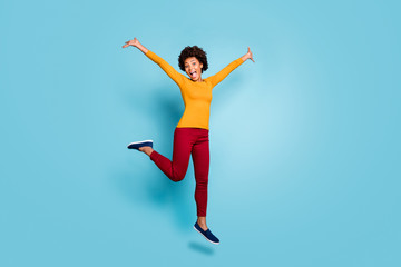 Fototapeta na wymiar Full length photo of funny dark skin lady jumping up high rejoicing spend vacation abroad addicted shopper wear yellow shirt red pants footwear isolated blue color background