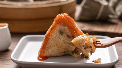 Rice dumpling zongzi eating - Young Asian woman is eating Chinese traditional food on wooden table at home for Dragon Boat Festival celebration, close up
