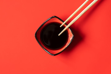 bowl of soy sauce and wooden chopsticks on red background. menu design template with space for text