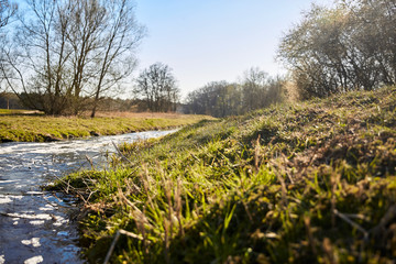 Colorful landscape with a beautiful curved stream with reflections, green meadow, blue sky in spring in Brandenburg, Germany