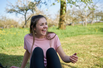 Obraz premium Young woman sitting in a meadow in spring laughing and having lots of fun in the background fruit trees
