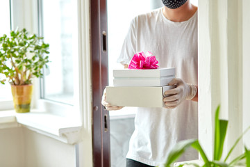 Courier man in white with protection medical mask and gloves contactless delivery presents, gift box during a coronavirus epidemic. Stay at home, Online shopping. Delivery service under quarantine..