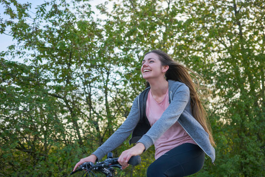 Young happily laughing woman with long hair riding a bike in beautiful greenery in springtime