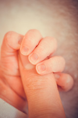 Touch of love. Close-up of baby's hand holding mother's finger. Newborn baby holding mother's hand, image with shallow depth of field.