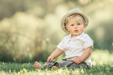 Cute little baby boy sitting on the grass in summer, on a Sunny day. Selective focus, space for text