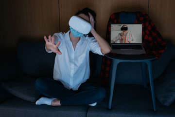 young woman outstretching hand, and boyfriend on screen of laptop eating popcorn while using vr headsets together