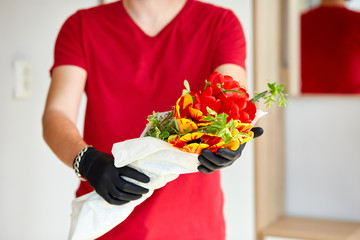 Courier, delivery man in red in medical gloves safely delivers online purchases a bouquet of flower during coronavirus epidemic. Stay home, safe concept. Contactless delivery service under quarantine.
