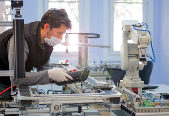 Man with surgical mask on face against COVID-19 ( Coronavirusis ) programming robot arm with...