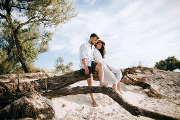 Happy young couple sitting on the beach on an old tree and hugging. Honeymoon at sea