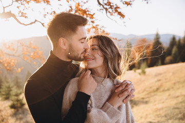 Stylish young couple in the autumn mountains. A guy and a girl hug together under a large old tree...