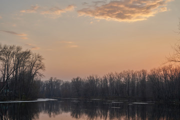    Early spring. Morning dawn over the lake in a misty, thoughtful haze. Beautiful view of the forest covered with fog early in the morning. The sun's rays of light.       