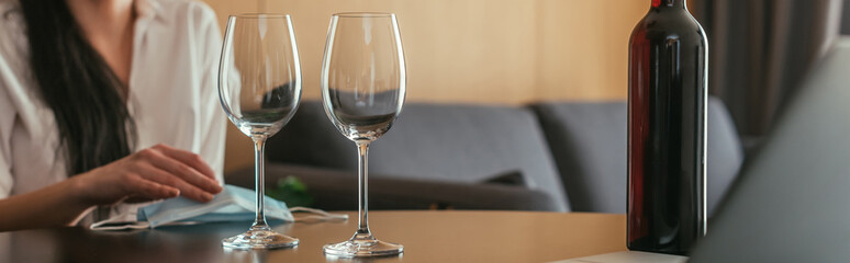 cropped view of woman near medical mask, wine glasses and bottle, horizontal image