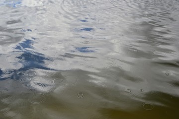 Raindrops on the water. Raindrops falling on the river surface. Sky and clouds reflection on the water.