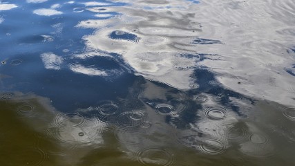 Raindrops on the water. Raindrops falling on the river surface. Sky and clouds reflection on the water.