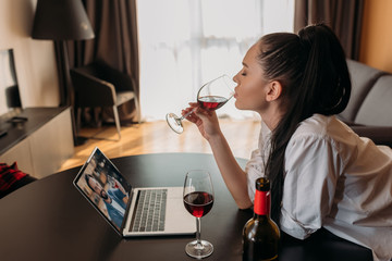 side view of young woman drinking red wine during video chat with boyfriend
