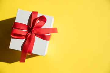 white gift box withred ribbon and bow on yellow background. Copy space.Fashion wrapped square gift or presents box, top view. Flat lay composition for birthday, christmas or wedding.