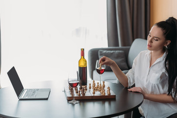 attractive woman playing chess near laptop with blank screen and red wine on table