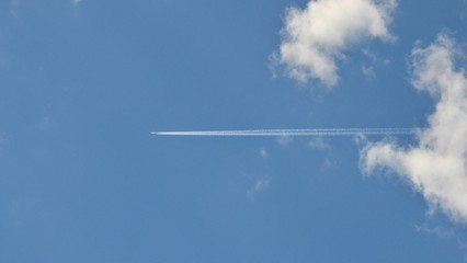Trace of an airplane in the blue sky. Jet airplane leaves contrails (or vapor trails, traces) on blue sky background. Travel, holidays, vacation concept