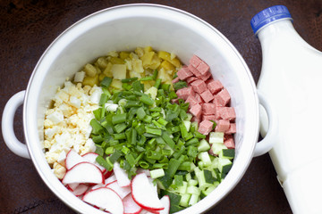 Okroshka with kefir. Russian dish. Sliced vegetables are visible in the pan. Nearby is a bottle of kefir. Shot from above.