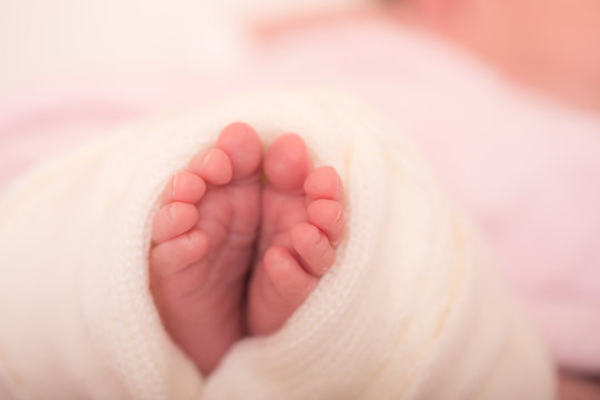Tiny foot of newborn baby. Soft newborn baby feet against a pink blanket. Baby girl feet with toes curled up.
