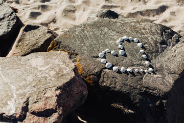 Heart shape made of sea pebbles and shells on sandy ocean beach, top view, copy space. Love summer vacation background, romance concept