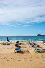 empty deck chairs by the sea, background with sea waves, sand and blue sky
