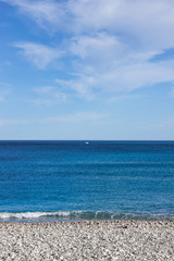 Fototapeta na wymiar landscape with sea, beach, blue sky and small white ship in distance, sunny day in Mediterranean