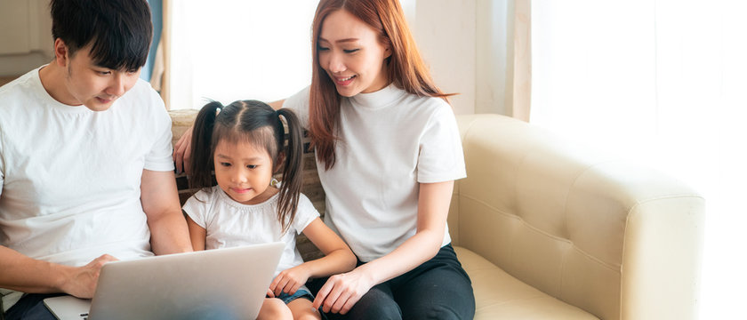Happy young Asian girl with her lovely parents using laptop computer for education and spent quality time together. Asian family, Social Distancing, homeschooling, work from home or new normal concept