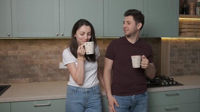 Just married couple drinks a coup of tea in the kitchen, on their new apartment, the are happy and hugs 