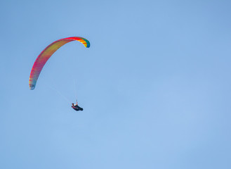 Orange and yellow paraglider on clear blue sky