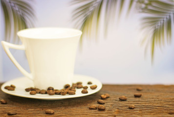a cup of coffee on wood on blurred palm leaf background
