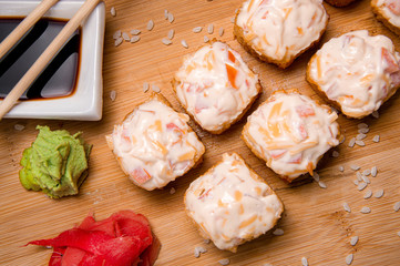 Fried rolls with a cap of vegetables and cheese sauce.
Wood background. White cup with sauce. Chinese chopsticks