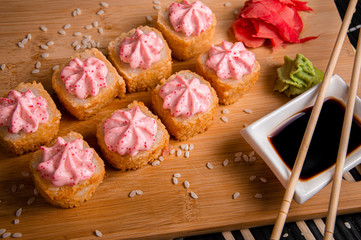 Fried rolls with pink hat made of sauce.
Wood background. White cup with sauce. Chinese chopsticks