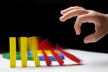Domino effect. Domino of colorful wooden blocks. Children's hand pushes dominoes on a white table....