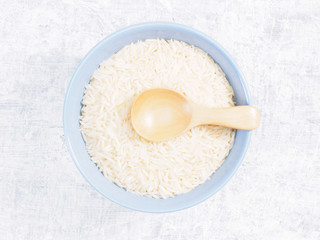 Indian long grain Basmati rice in blue ceramic bowl and wooden spoon on white concrete background