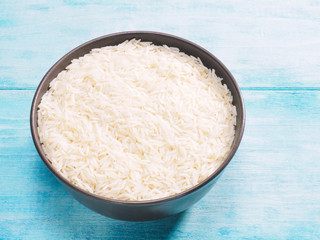 Long grain Basmati rice in brown ceramic bowl on blue wooden background