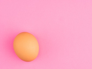One brown chicken egg on a pink background with copy space. Healthy eating concept