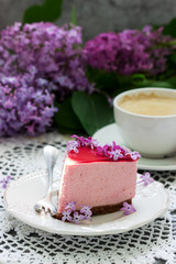 A berry mousse cake with chocolate base and juice jelly, decorated with lilac flowers, served with coffee.