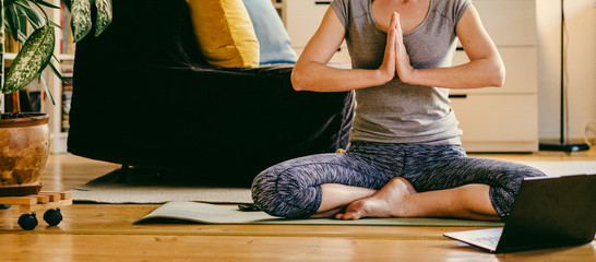 woman doing yoga workout at home watching videos online on laptop computer