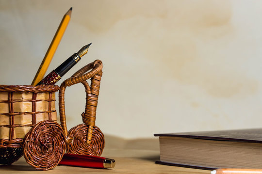 The concept of antiquity. Image for caption. Against the background of old paper lies a book, a wicker basket in the form of a bicycle and in it a pencil and pen - Powered by Adobe