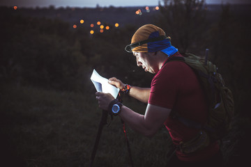 The guy during night orienteering shines a flashlight in a map of the area