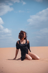 A girl in a black swimsuit sits on the sand in the desert
