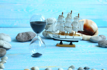 Fototapeta na wymiar Banner with beach accessories on a blue board aquamarine color background - hourglass, boat, sea ​​stones. Summer. Concept of summer holidays. Vacation and Travel Time Concept.
