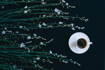 Coffee and flowers. Composition of wild spring tender flowers and cup of coffee on black background.  Spring coffee concept. Top view. Flat lay. Good morning.