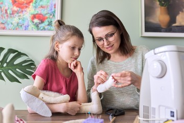 Happy mother and daughter sewing together toy bunny doll at home