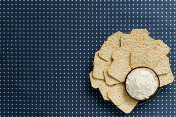 A plate with crackers and curd cheese lying on a polka dot tablecloth.